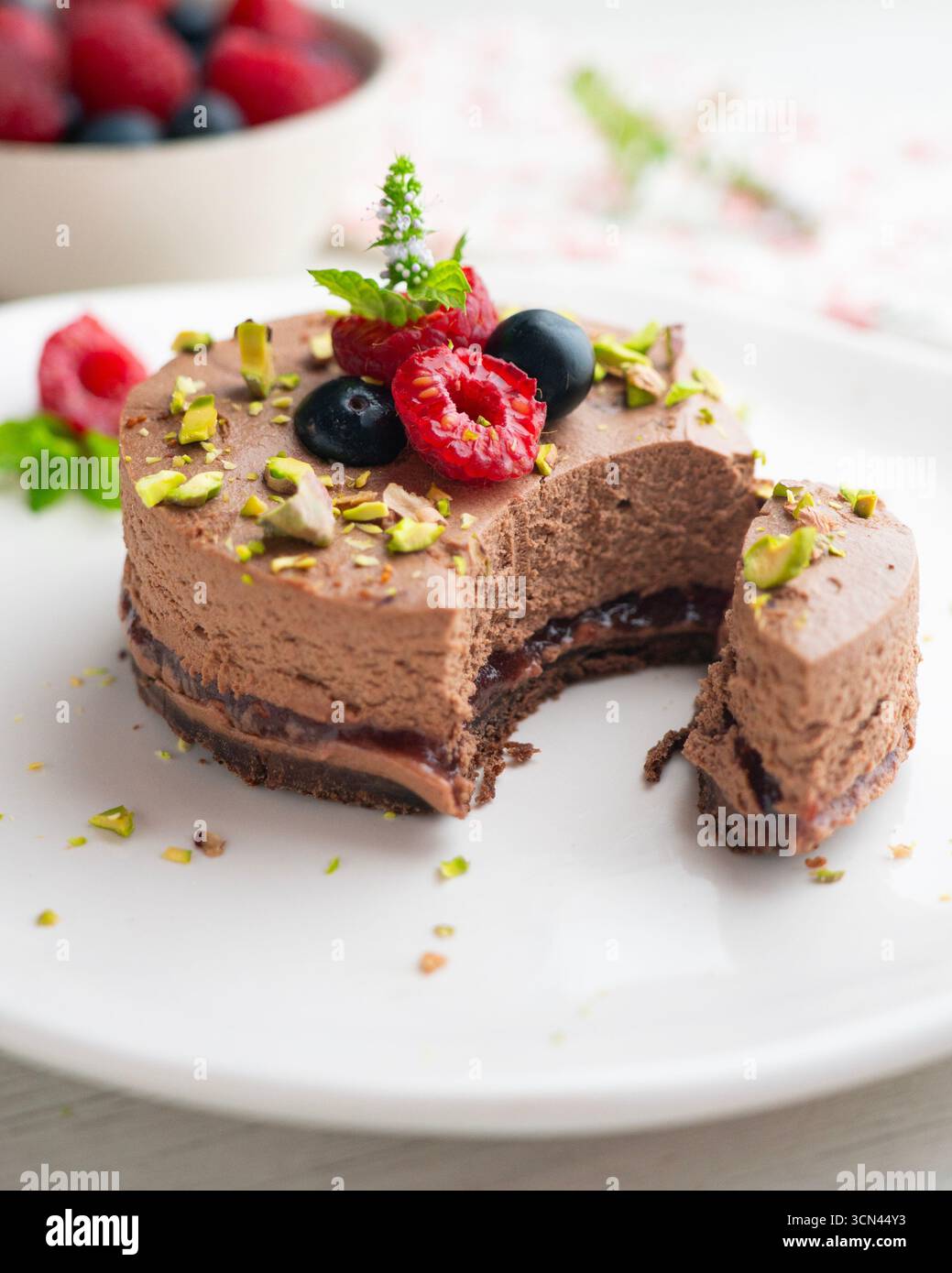 Crostata con mousse al cioccolato ripiena di marmellata e decorata con pistacchi e frutti di bosco rossi. Foto Stock