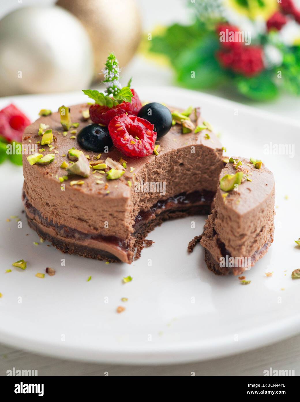 Crostata con mousse al cioccolato ripiena di marmellata e decorata con pistacchi e frutti di bosco rossi. Foto Stock