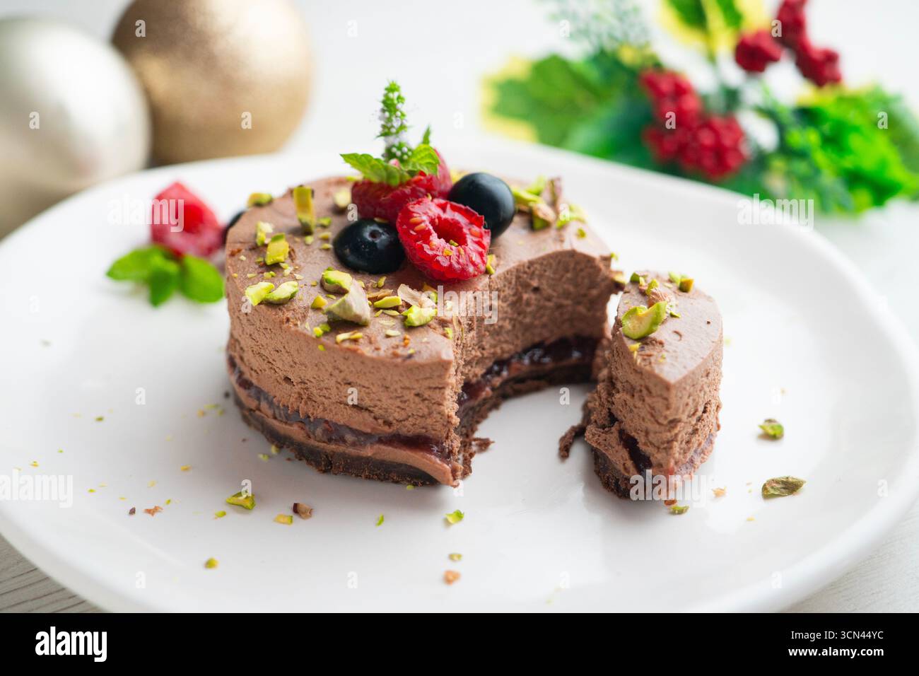 Crostata con mousse al cioccolato ripiena di marmellata e decorata con pistacchi e frutti di bosco rossi. Foto Stock