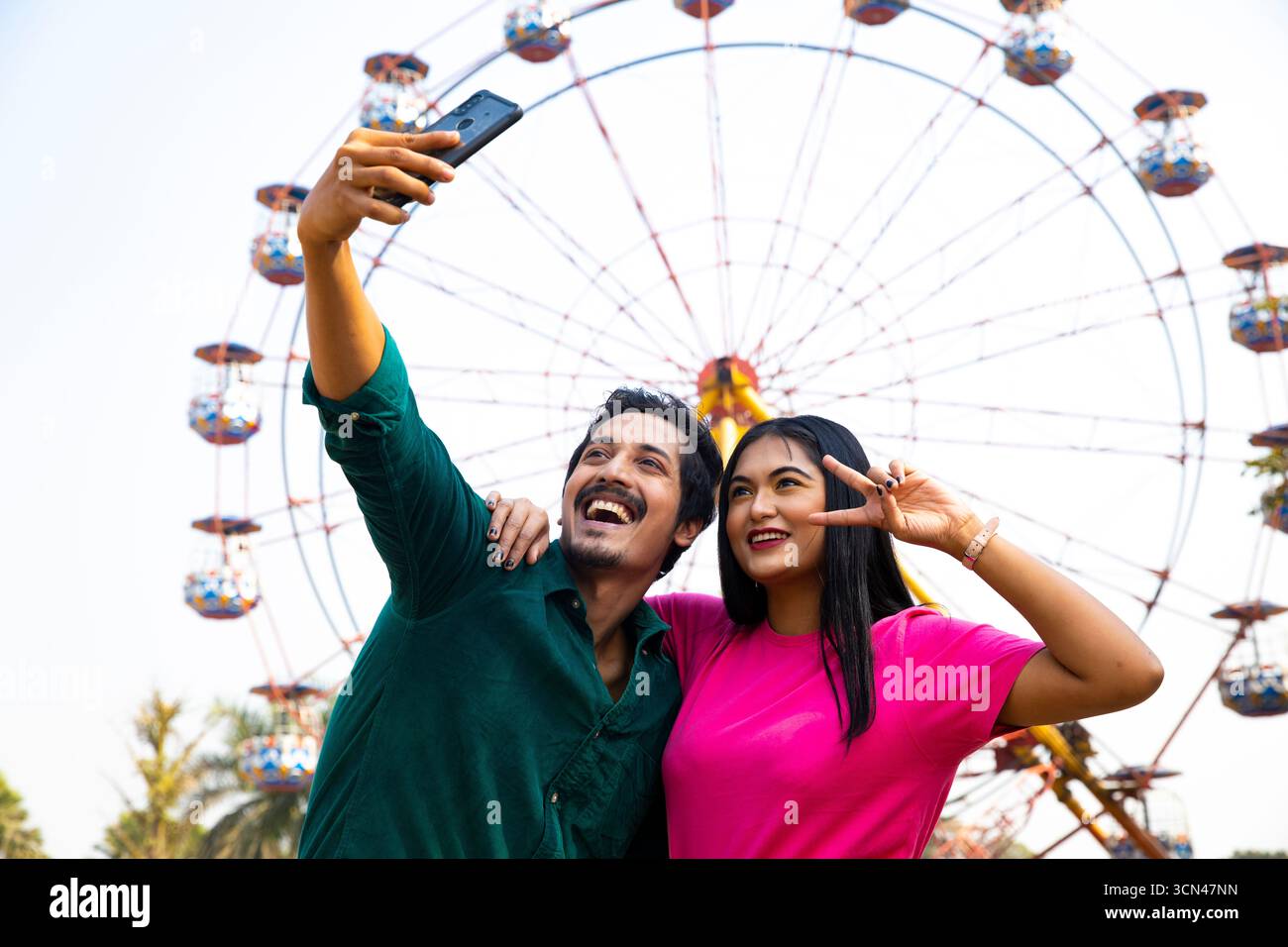 Coppia che porta Selfie davanti alla ruota panoramica - momento divertente del parco divertimenti Foto Stock