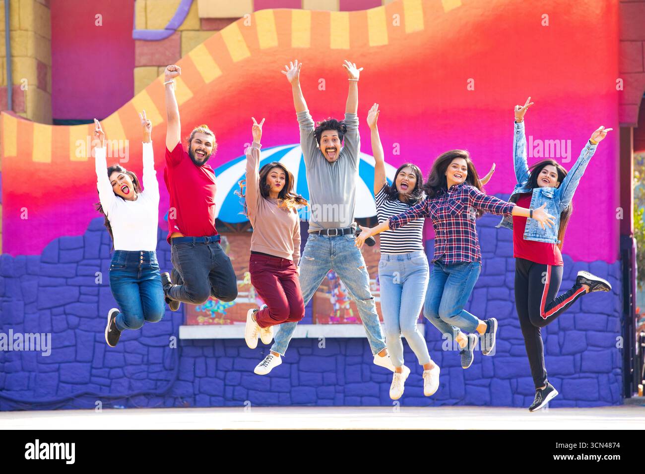 Gruppo di amici che saltano per la gioia davanti a una parete colorata - momenti divertenti all'aperto Foto Stock