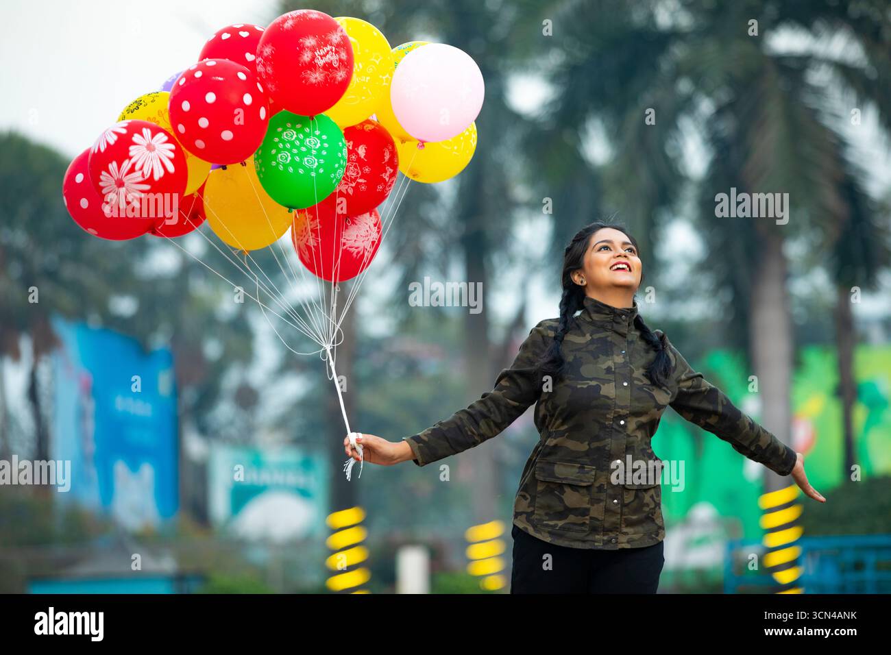 Donna gioiosa che tiene in mano palloncini colorati nel parco divertimenti - vibrante momento all'aperto Foto Stock