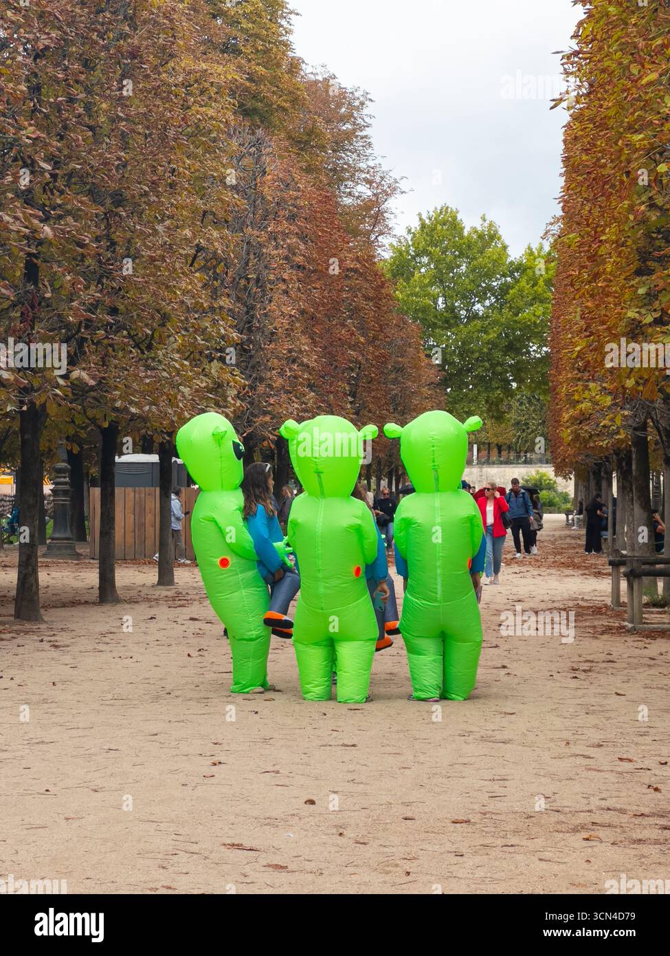 Parigi, Francia - 13 settembre 2025: Un gruppo in costumi alieni gonfiabili si erge su un sentiero di ghiaia nel Giardino delle Tuileries, fiancheggiato da alberi autunnali. Foto Stock