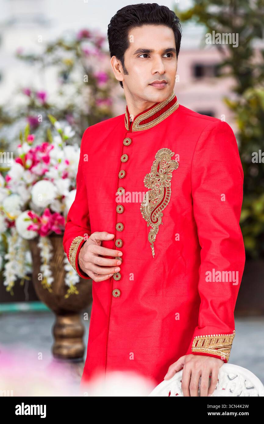 Sherwani Regal ricamati in rosso e oro per spigoli | abbigliamento da sposa indiano pakistano di lusso | abbigliamento formale firmato da uomo tradizionale Foto Stock