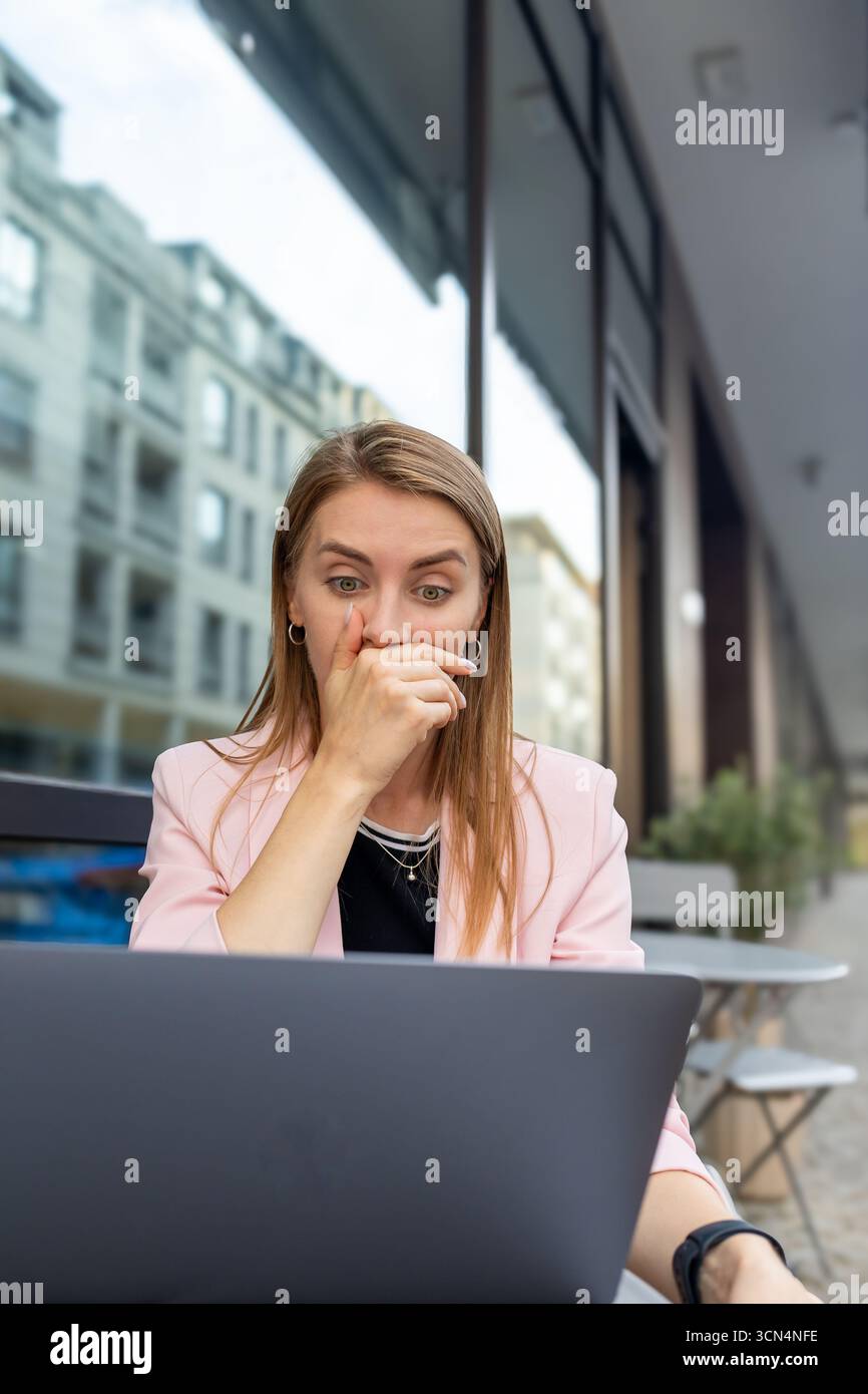 donna sorpreso che guardasse lo schermo di un notebook seduto sulla terrazza del caffè Foto Stock