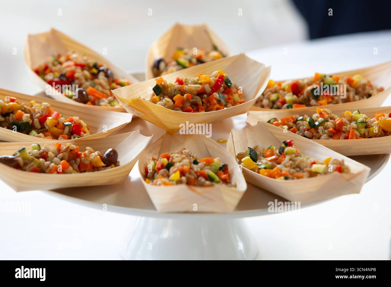 Piccoli vassoi in legno contenenti insalata di orzo con verdure miste, disposti su un piedistallo bianco, pronti per un evento di catering Foto Stock