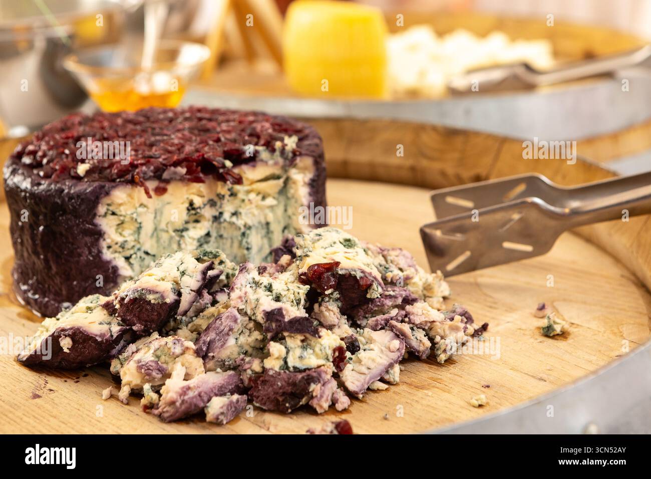 Fette di formaggio blu con copertura rossa siediti su una tavola di legno con pinze da portata, pronte per la degustazione Foto Stock