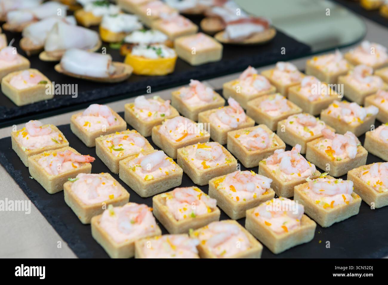 File di bocche quadrate riempite di gamberi e salsa, creando un'elegante e appetitosa esposizione per un evento con catering Foto Stock
