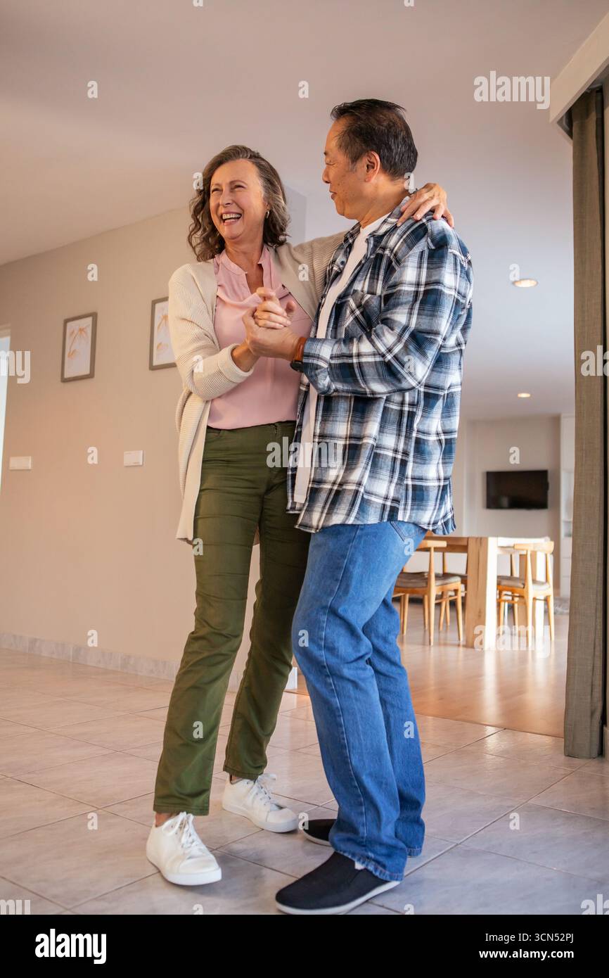 Diverse coppie che ballano allegramente nell'area soggiorno open space vicino a un tavolo in legno e stampe incorniciate Foto Stock