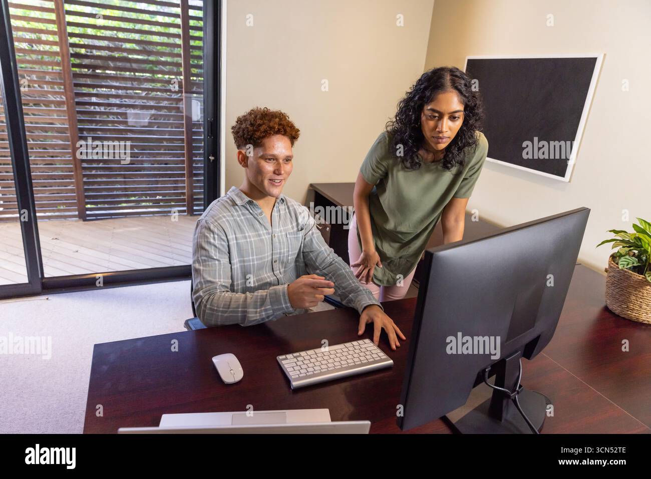 Diversi colleghi che collaborano alla scrivania in ufficio utilizzando monitor, tastiera e mouse da scrivania Foto Stock