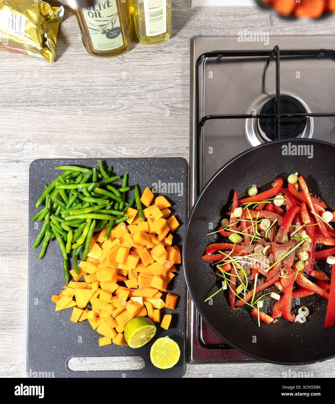 Vista dall'alto di un piano cottura con verdure a fette, tra cui peperone rosso, fagiolini e zucca accanto a una teglia da cucina su un piano cottura Foto Stock