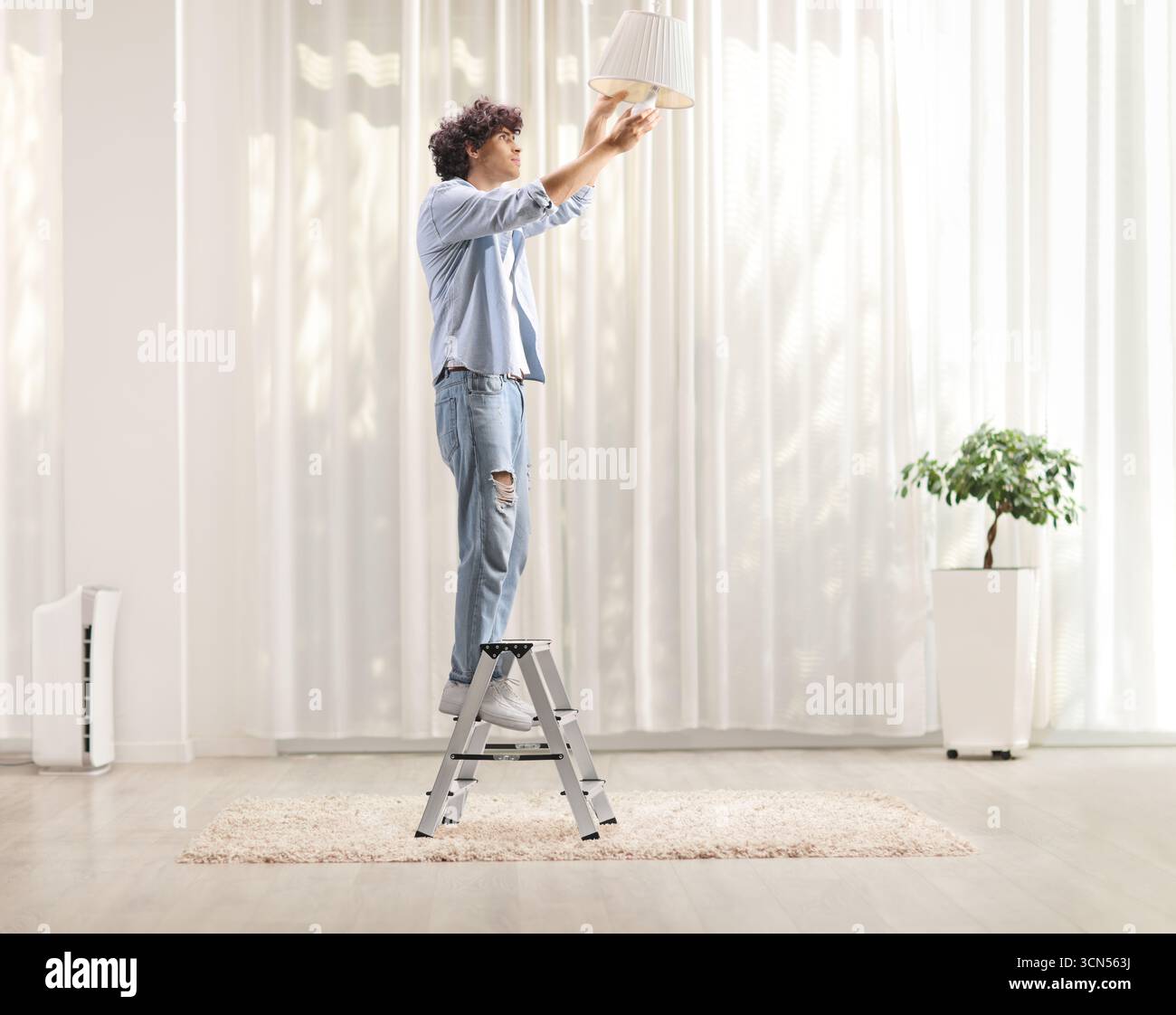 Uomo in piedi su una scala e che cambia una lampadina in una stanza Foto Stock
