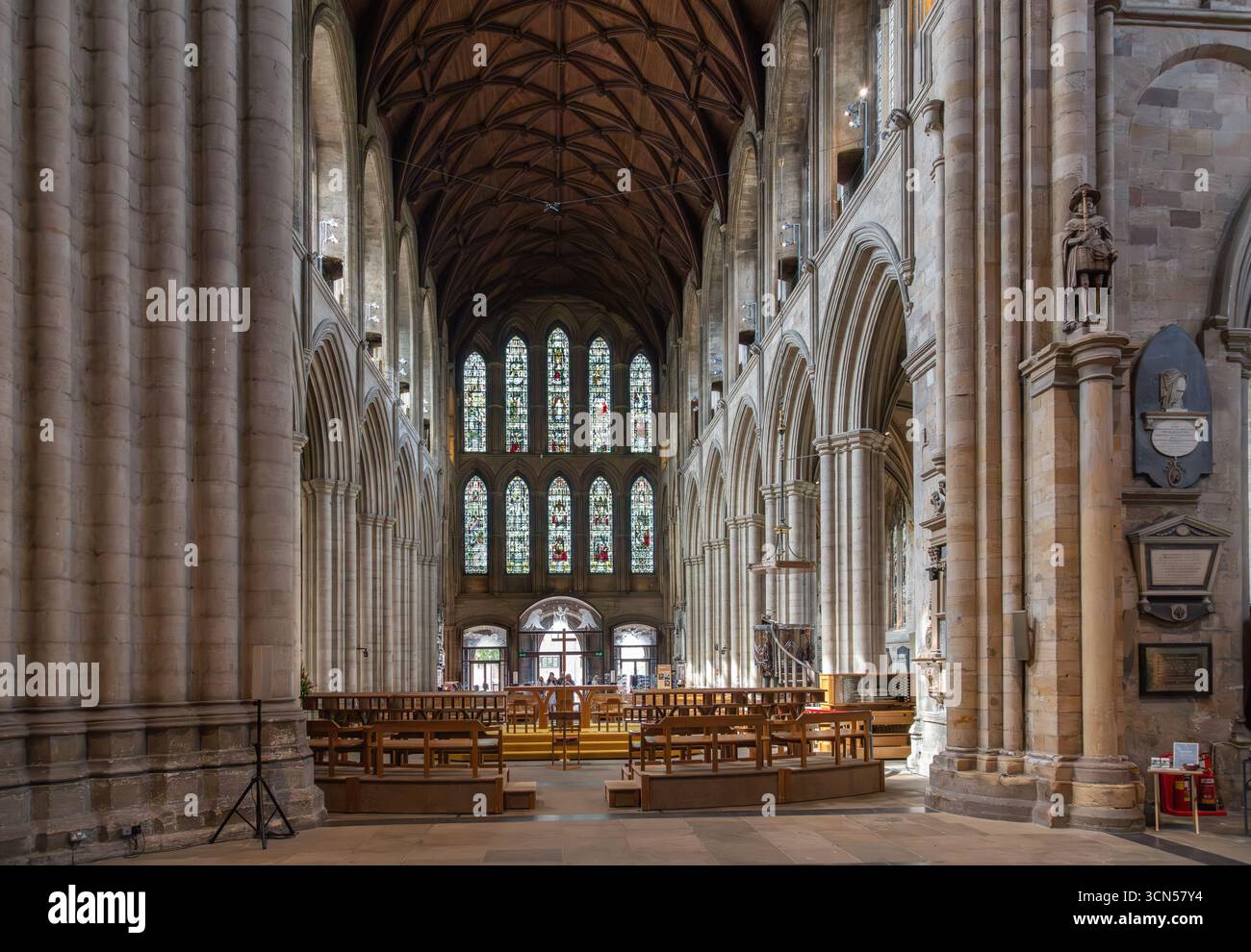 Vista interna della Cattedrale di Ripon, nel North Yorkshire, con archi romanici, volte a coste, vetrate colorate e pali di legno nella chiesa storica Foto Stock