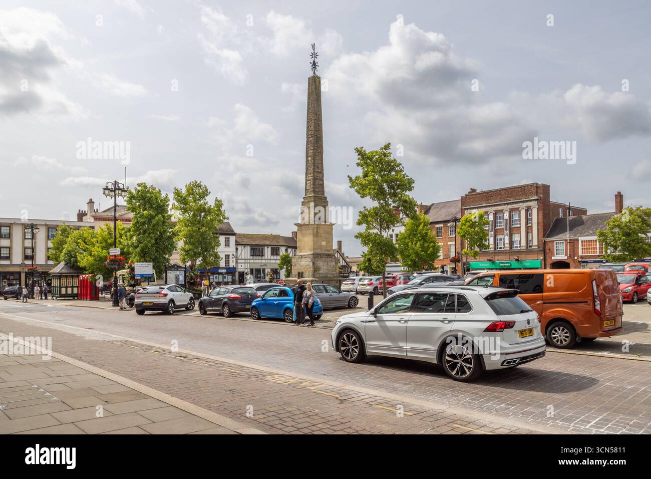 L'obelisco di Ripon nella piazza del mercato, North Yorkshire, un monumento classificato Grade i costruito nel 1702, circondato da negozi, alberi e pedoni Foto Stock