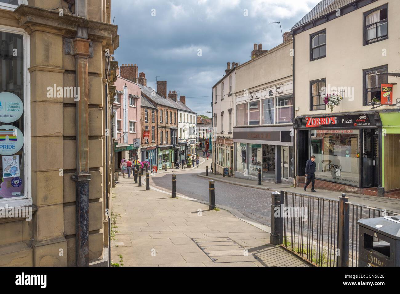 Negozi lungo Kirkgate a Ripon, North Yorkshire, tra cui Zorbas Pizza e aziende locali, visti su una strada lastricata nel centro della città Foto Stock