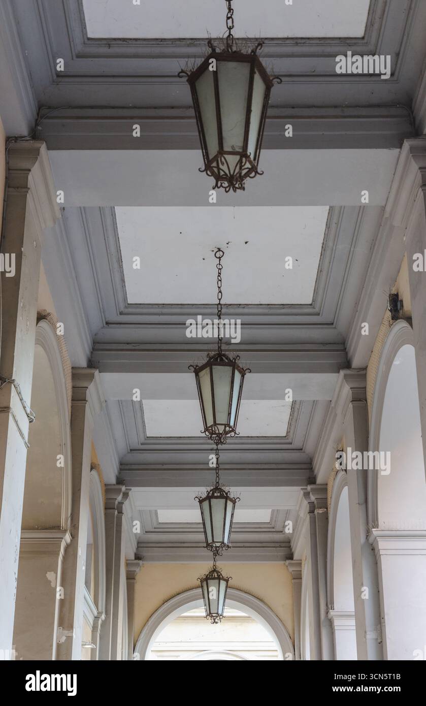 Vista delle lanterne ornate appese elegantemente dal soffitto a volta di un colonnato, che proietta luce e ombre soffuse, creando un ambiente sereno, Chieti, Abruzzo, Italia. Foto Stock