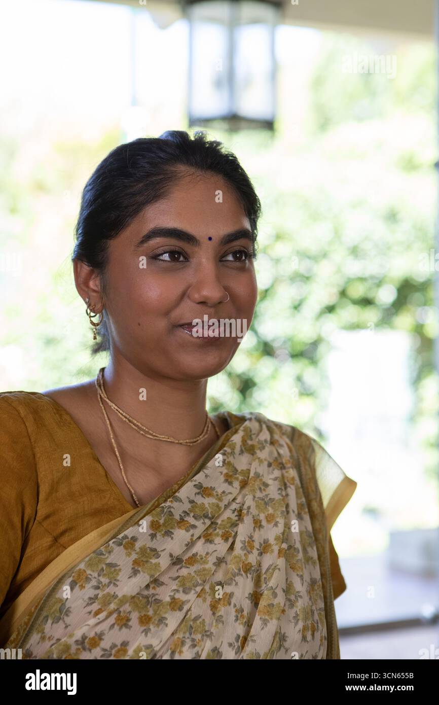 Donna indiana che indossa camicetta di senape sari bindi naso anello, ornamenti su veranda sotto lanterna Foto Stock