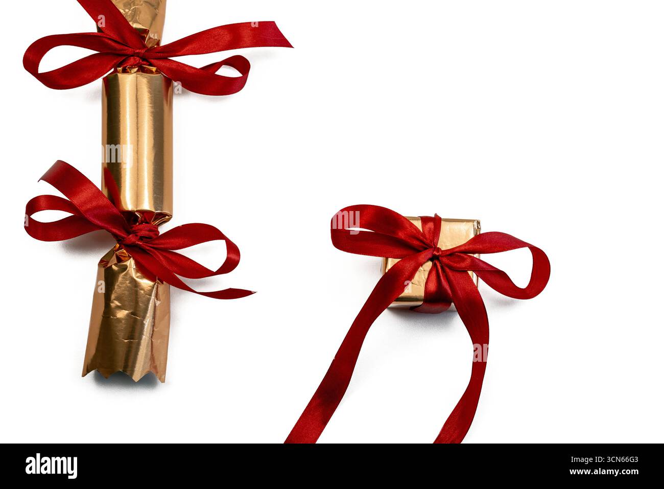 Un cracker natalizio dorato realizzato a mano con nastri di raso rosso e un regalo avvolto in carta dorata lucida su sfondo bianco. Copia spazio Foto Stock