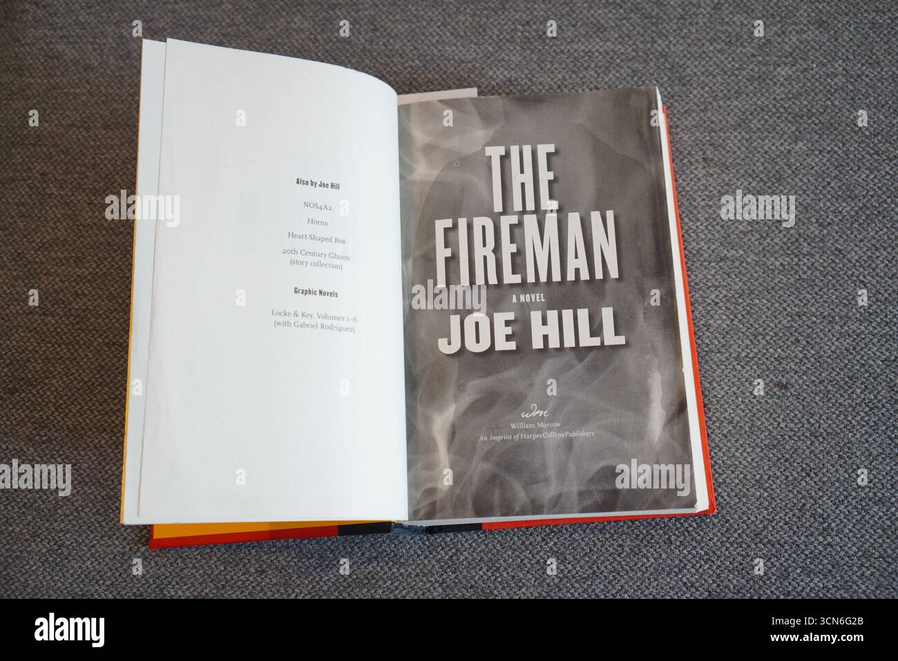 Un libro aperto intitolato "The Fireman" di Joe Hill con una copertina grigia a tema fumé e testo visibile sulla pagina del titolo. Foto Stock