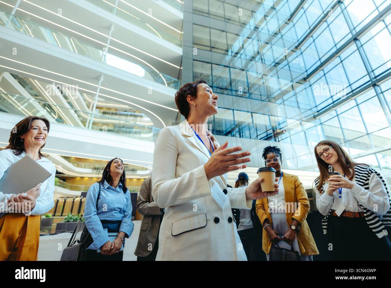 Una fiduciosa dirigente femminile accoglie un gruppo di nuovi assunti in una moderna lobby di uffici all'aperto. Si impegna calorosamente, creando un ambiente inclusivo e positivo Foto Stock