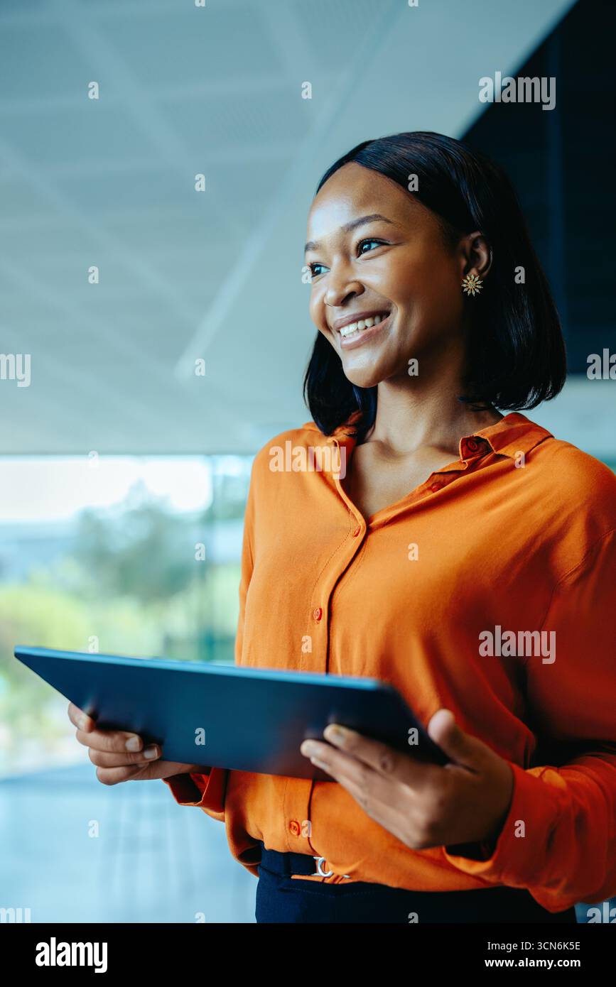 Ritratto di una donna d'affari sicura che tiene un tablet in un ufficio moderno. Sorridente e pronto, incarna professionalità e successo. Idea Foto Stock