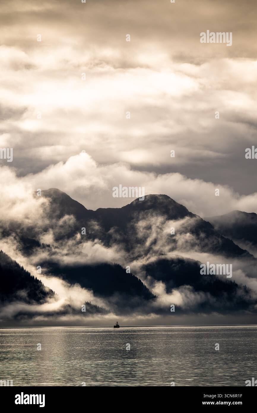 Una barca nella Resurrection Bay vicino a Seward, Alaska, è sminuita dalle montagne durante un pomeriggio nuvoloso. Foto Stock