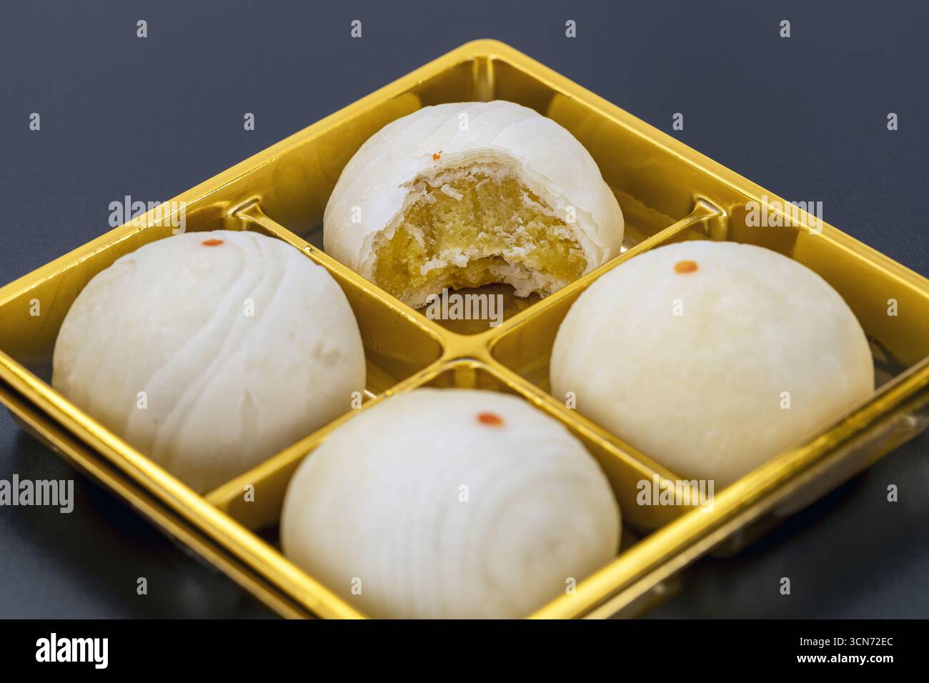 Una torta cinese di mooncake ripiena di pasta di fagioli, una con morso preso, esposta su un vassoio dorato, che presenta dessert tradizionali con consistenza morbida e dolce Foto Stock