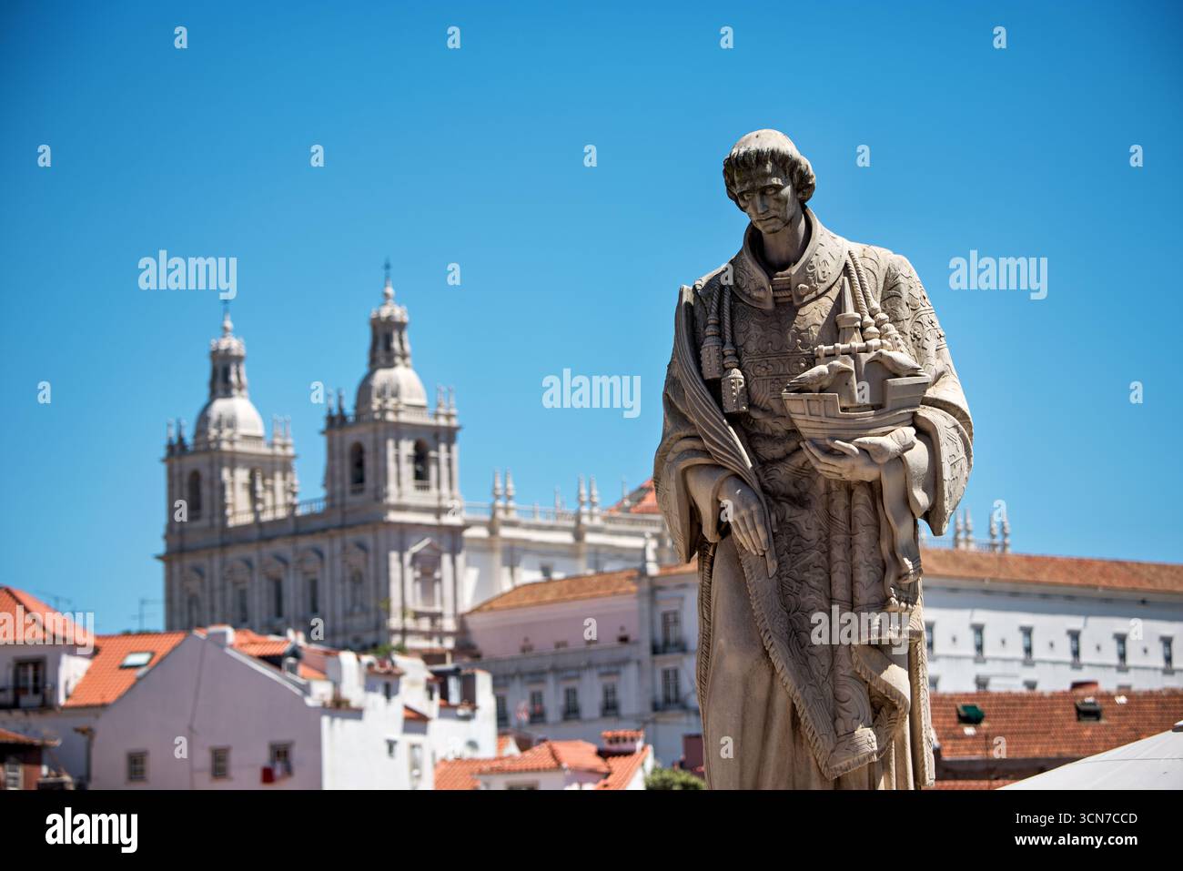 Statua di San Vincenzo Miradouro Das Portas do Sol Lisbona Portogallo // LISBONA, Portogallo — la statua di San Vincenzo (São Vicente) si trova nel punto panoramico di Miradouro das Portas do Sol nello storico quartiere di Alfama. Scolpita in pietra calcarea leggera, la statua raffigura San Vincenzo di Saragossa, martire cristiano del IV secolo e santo patrono di Lisbona, con una nave modello in stile caracca. Questa nave simboleggia le navi che, secondo la leggenda, trasportarono le sue reliquie in città nel XII secolo. Il santo è mostrato in elaborate vesti liturgiche, facendo riferimento ai suoi ruoli di diacono e martire. Foto Stock