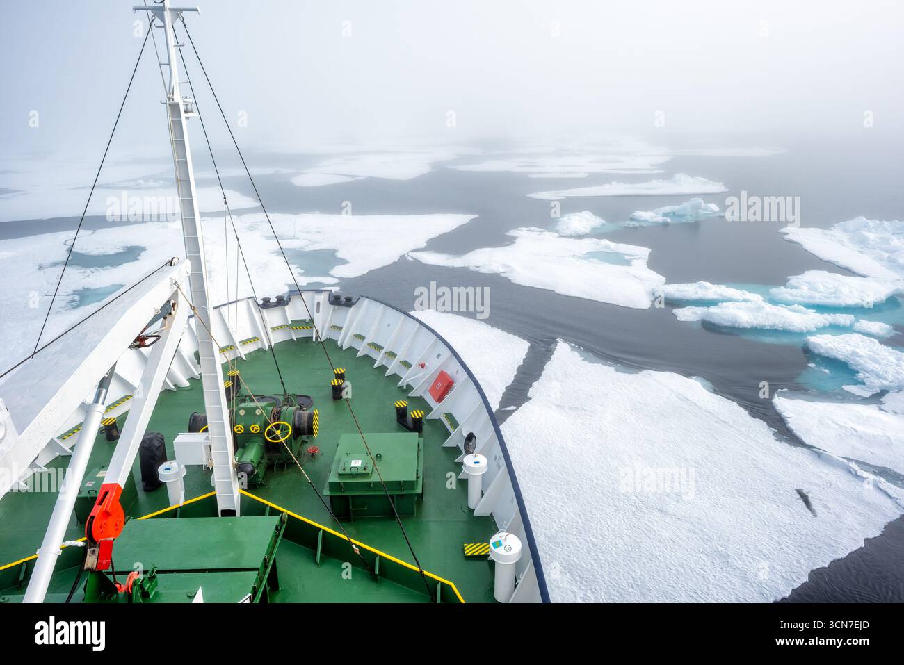Nave nell'Oceano Artico con i banchi di ghiaccio Svalbard Norvegia // SVALBARD, Norvegia - Una nave naviga attraverso l'Oceano Artico, circondata da numerosi banchi di ghiaccio. La prua dell'imbarcazione è visibile, con attrezzature da ponte, tra cui verricelli e attrezzature di sicurezza. Le acque circostanti sono un mix di oceano scuro e ghiaccio galleggiante, con alcuni ruscelli che mostrano un'impressionante tonalità turchese. Questa scena cattura l'ambiente impegnativo ma maestoso dell'arcipelago delle Svalbard, un territorio norvegese situato tra la Norvegia continentale e il Polo Nord, noto per le sue popolazioni di orsi polari e i ghiacciai. Foto Stock