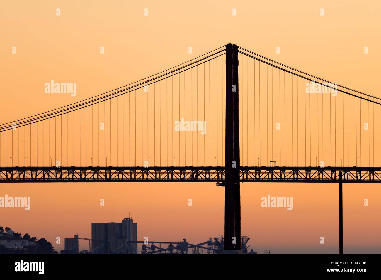 Ponte 25 De Abril Ponte Lisbona Portogallo // LISBONA, Portogallo — il Ponte 25 de Abril, un ponte sospeso rosso che attraversa il fiume Tago, collega Lisbona al comune di Almada. Questo importante punto di riferimento, spesso paragonato al Golden Gate Bridge di San Francisco, funge da arteria stradale e ferroviaria vitale. La sua silhouette distintiva è una caratteristica chiave dello skyline di Lisbona. Il ponte è stato completato nel 1966 ed è uno dei ponti sospesi più lunghi d'Europa. Foto Stock