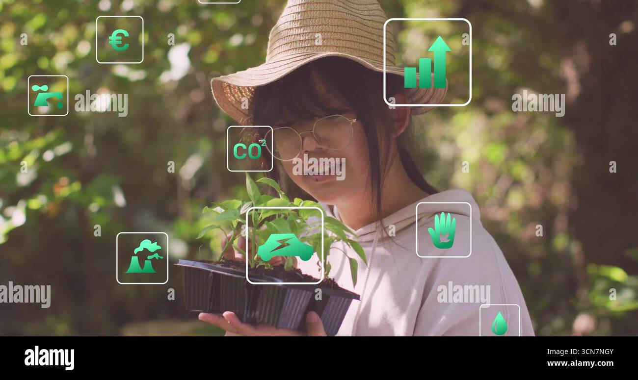 Ragazza cinese che indossa un cappello di paglia e occhiali rotondi che reggono un vassoio di piantine in giardino, con icone verdi Foto Stock