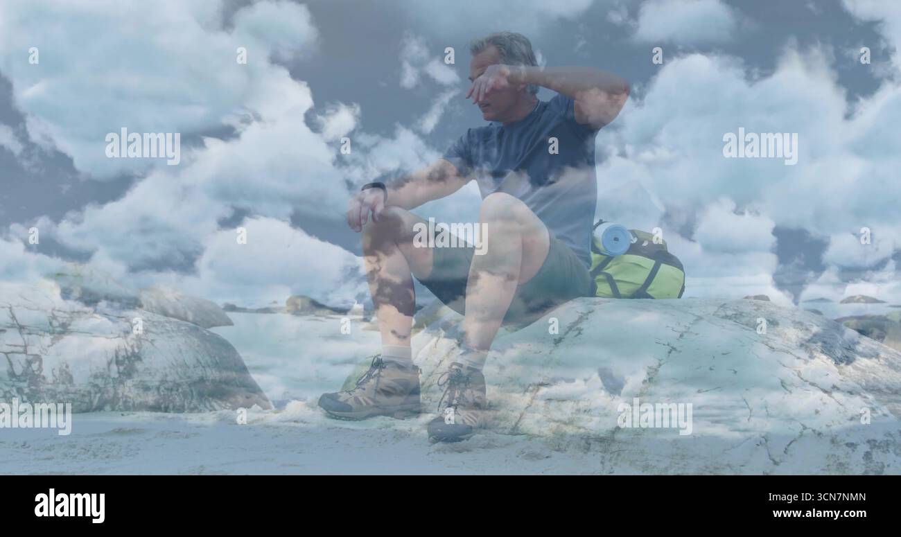 Riposa l'escursionista di mezza età che protegge gli occhi mentre è seduto sulle rocce costiere, con uno zaino verde brillante Foto Stock