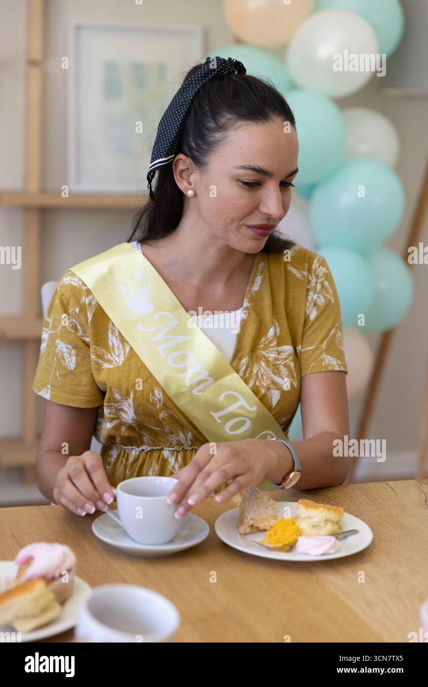 Donna incinta che indossa un vestito giallo con la mamma che deve tenere la pasta al tavolo della doccia del bambino Foto Stock