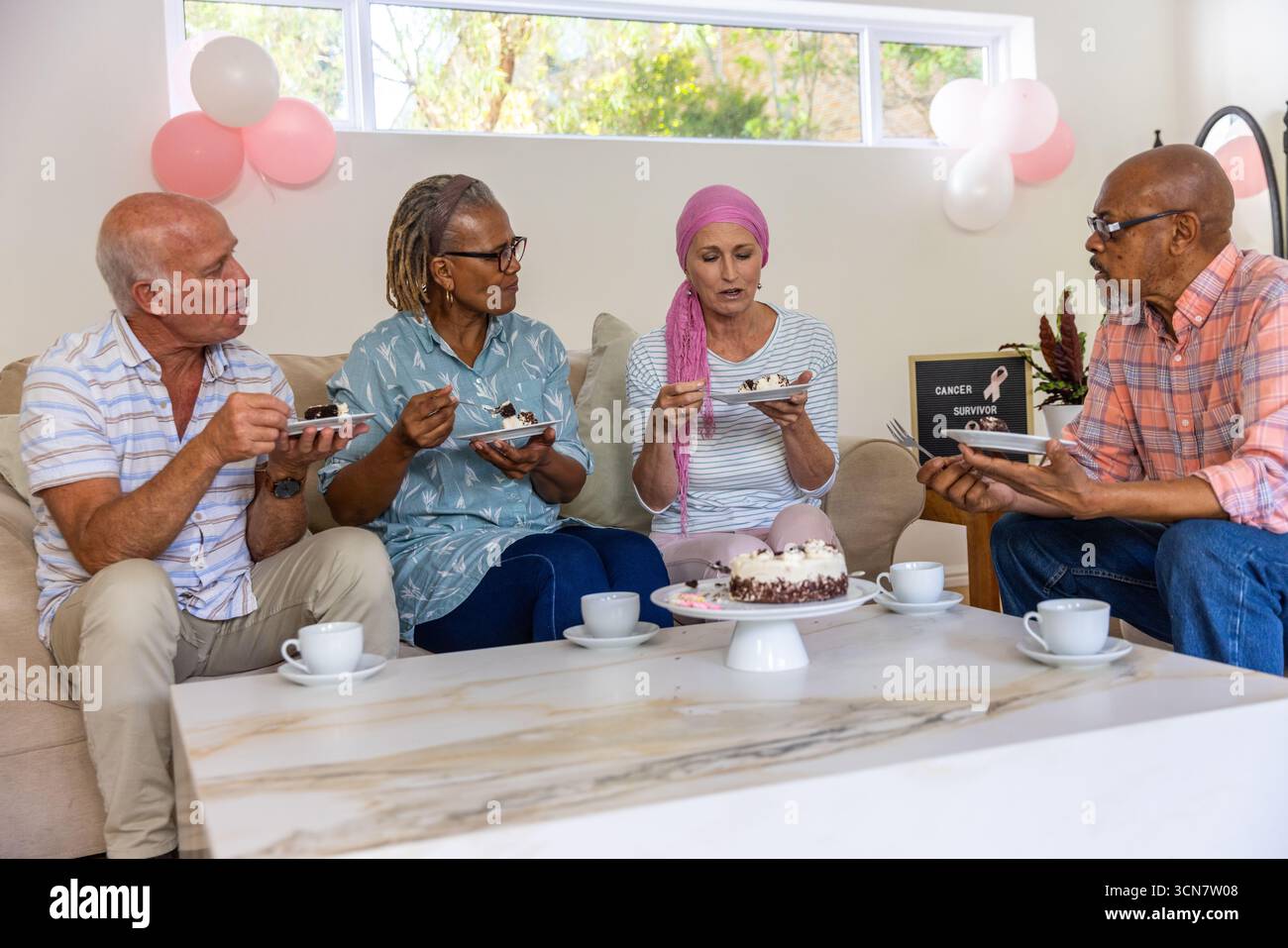Amici diversi che festeggiano in salotto con torta sul tavolino da caffè, segno di sopravvissuto al cancro Foto Stock