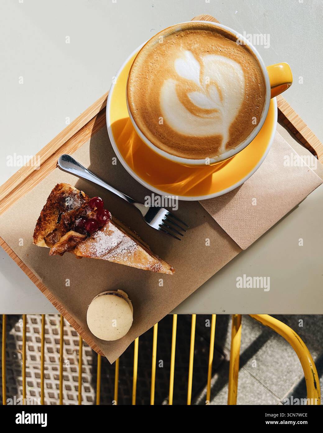Un delizioso bicchierino dall'alto di un buon caffè e dessert abbinati. Una bella tazza di cappuccino con delicata latte art viene servita su un piattino giallo Foto Stock