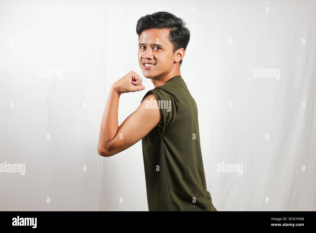 Giovane sicuro di sé che si flette bicipiti con un sorriso, mostrando fitness e salute per i contenuti lifestyle Foto Stock