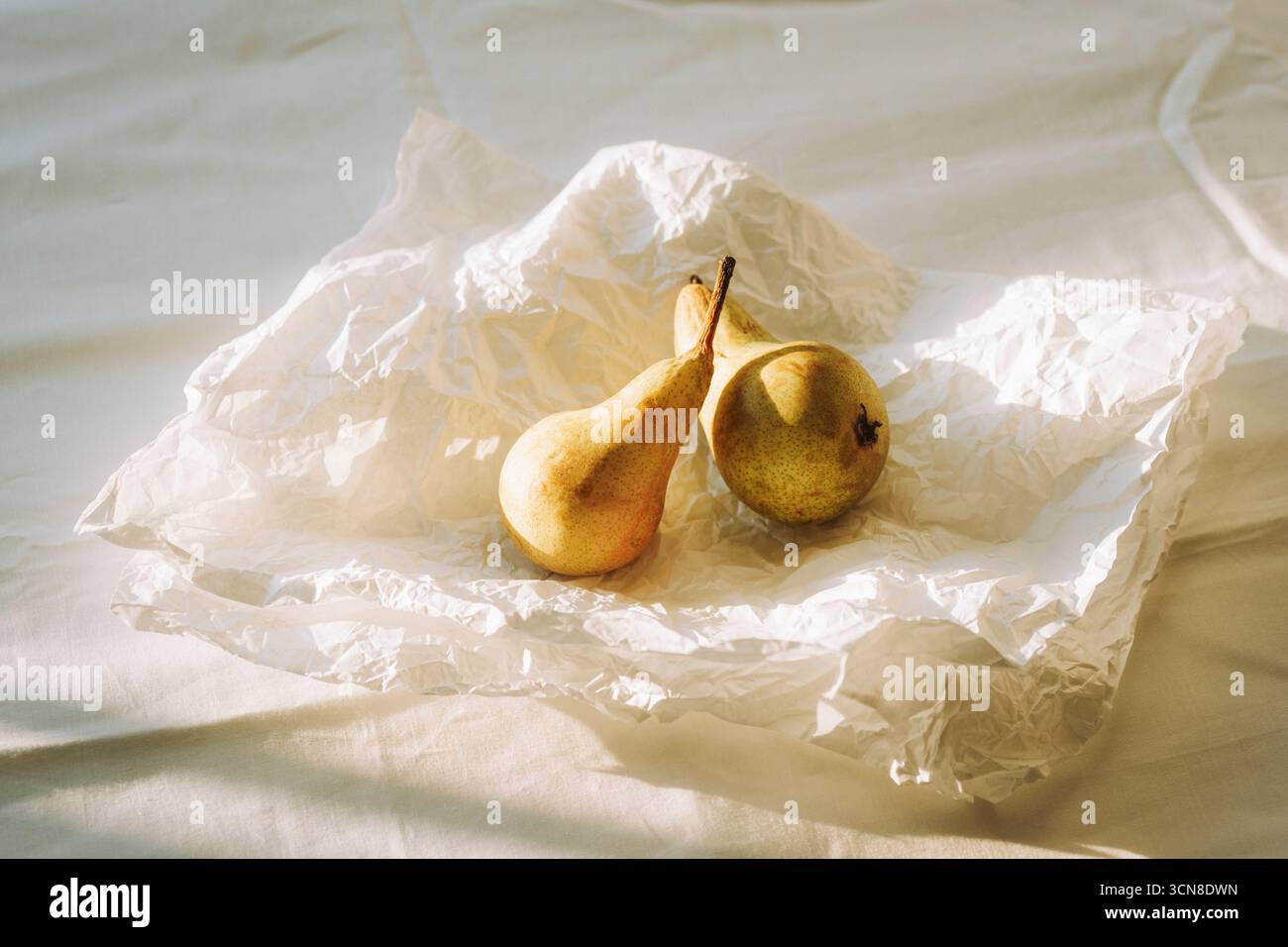 Due pere mature su carta bianca sgualcita in una luce naturale soffusa. Foto Stock