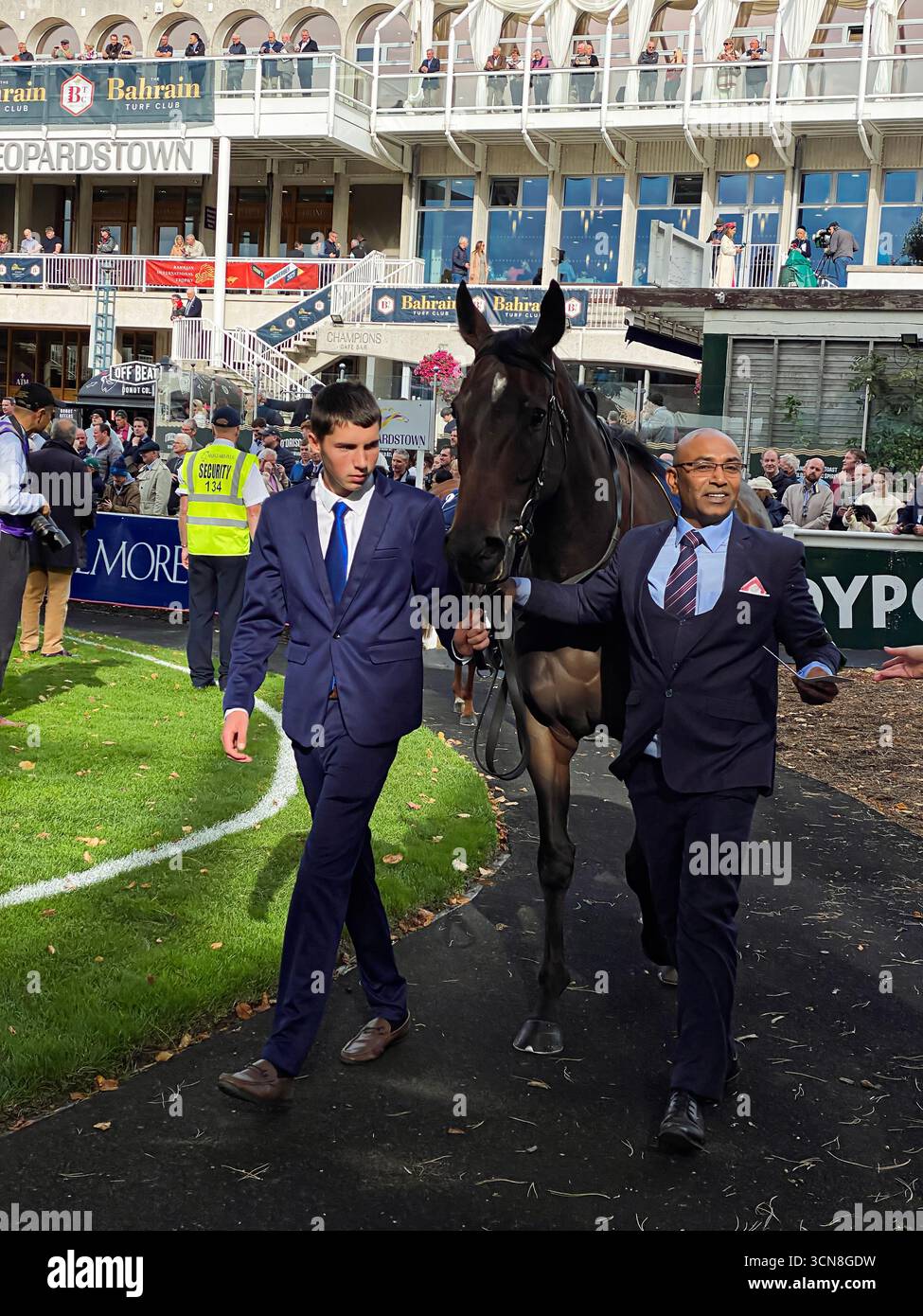 Irish Champions Festival, ippodromo di Leopardstown, Dublino, Irlanda. Maneggiatori, fantini e purosangue nel paddock prima della gara. - Immagine stock catturata con smartphone