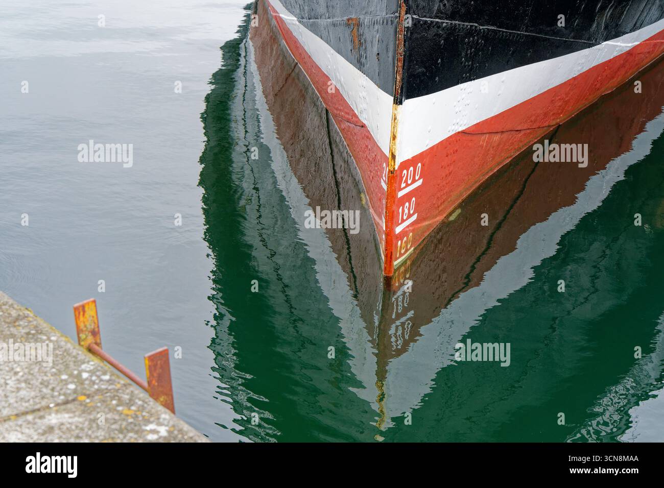 Una scenografia del porto avvolgente incornicia un fiocco nero con una sottile linea bianca e un'ampia fascia rossa. La vernice graffiata e la ruggine mostrano i suoi anni. Segni 200, 180, 160 salita t Foto Stock