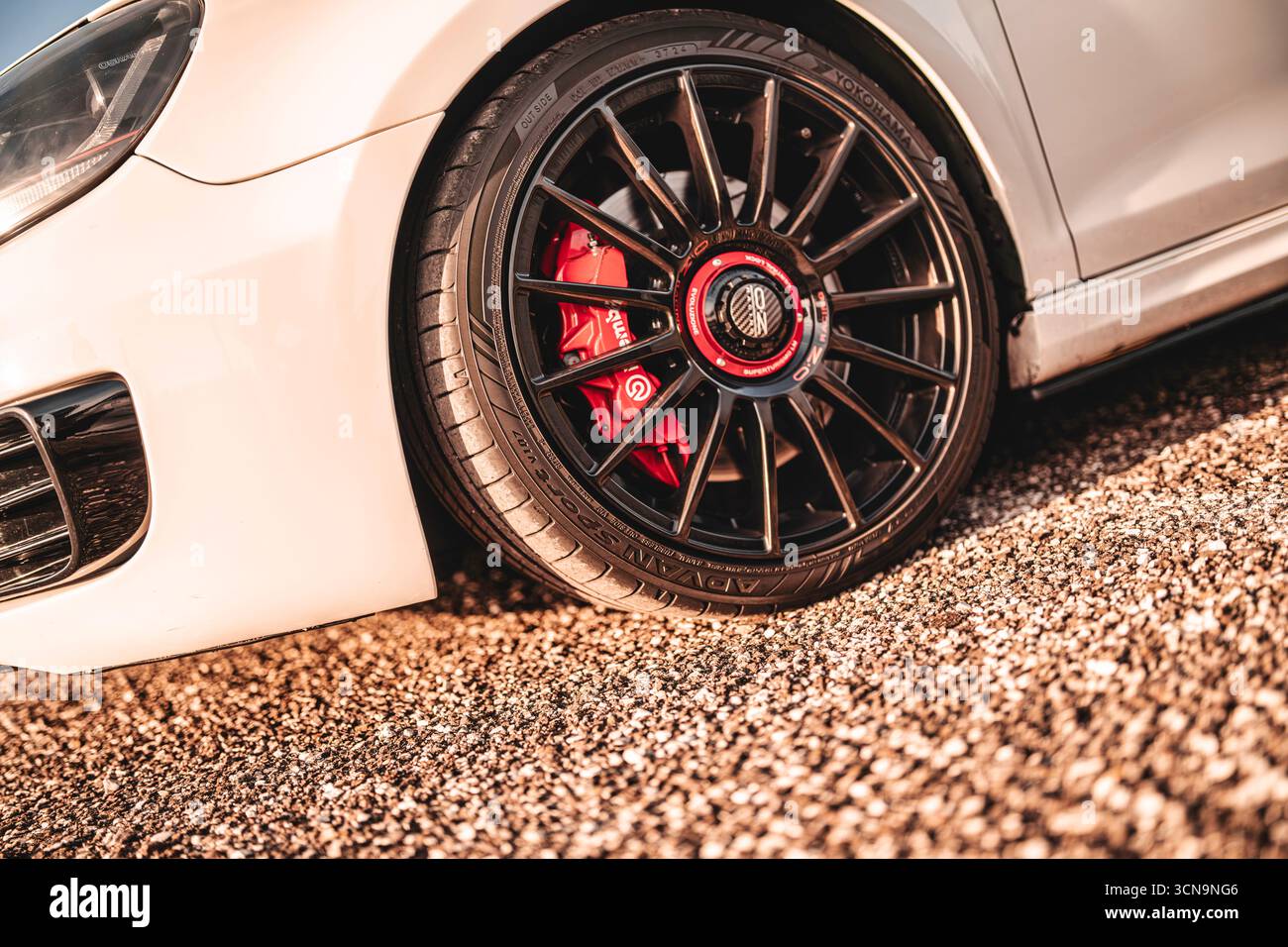 Milano, italia 20 settembre 2025: Auto sportiva bianca in piedi su ghiaia con cerchioni neri personalizzati, pneumatici a profilo basso e pinze dei freni rosse ad alte prestazioni Foto Stock