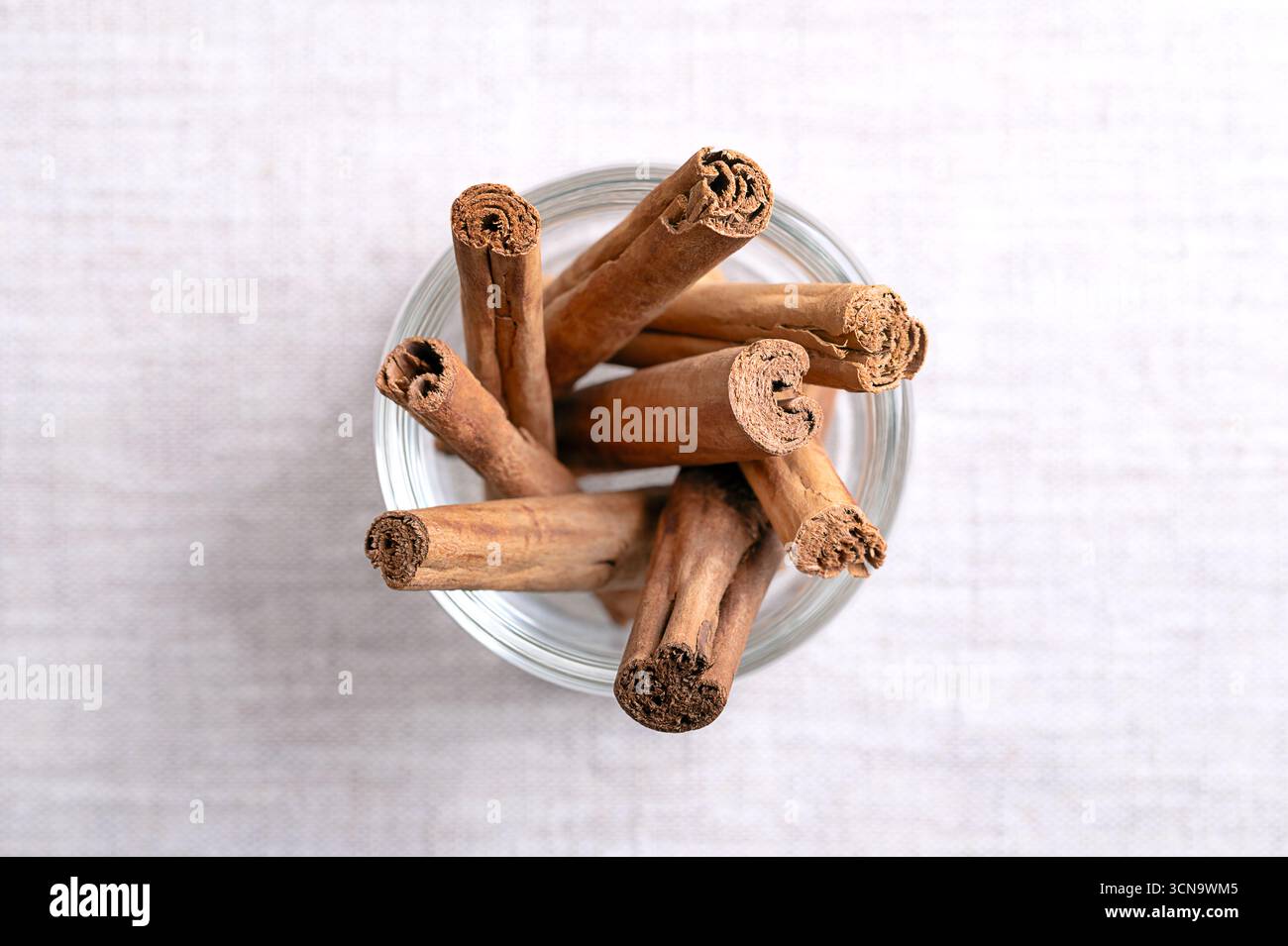 Strisce di corteccia di cannella di Ceylon essiccate, in un bicchiere, su lino. Cortecce intere essiccate di Cinnamomum verum. Foto Stock