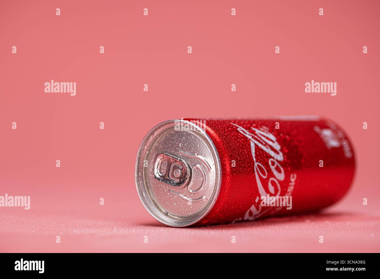 Una lattina di Coca-Cola è seduta su una superficie rosa. La bomboletta è aperta e presenta condensa Foto Stock