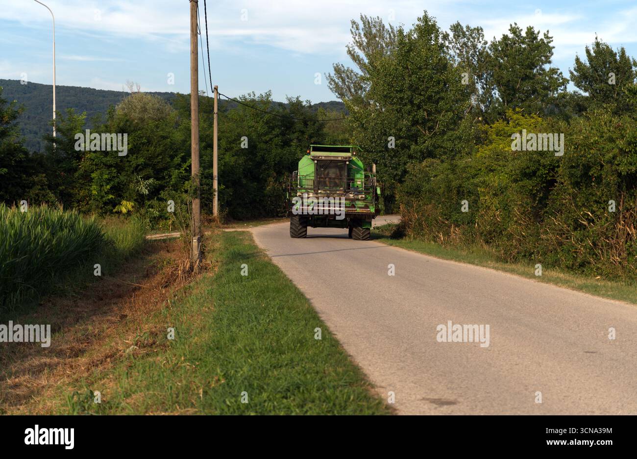 Una grande mietitrebbia verde percorre una strada di campagna stretta e tortuosa, lasciando una piccola scia di polvere sul suo percorso. Foto Stock