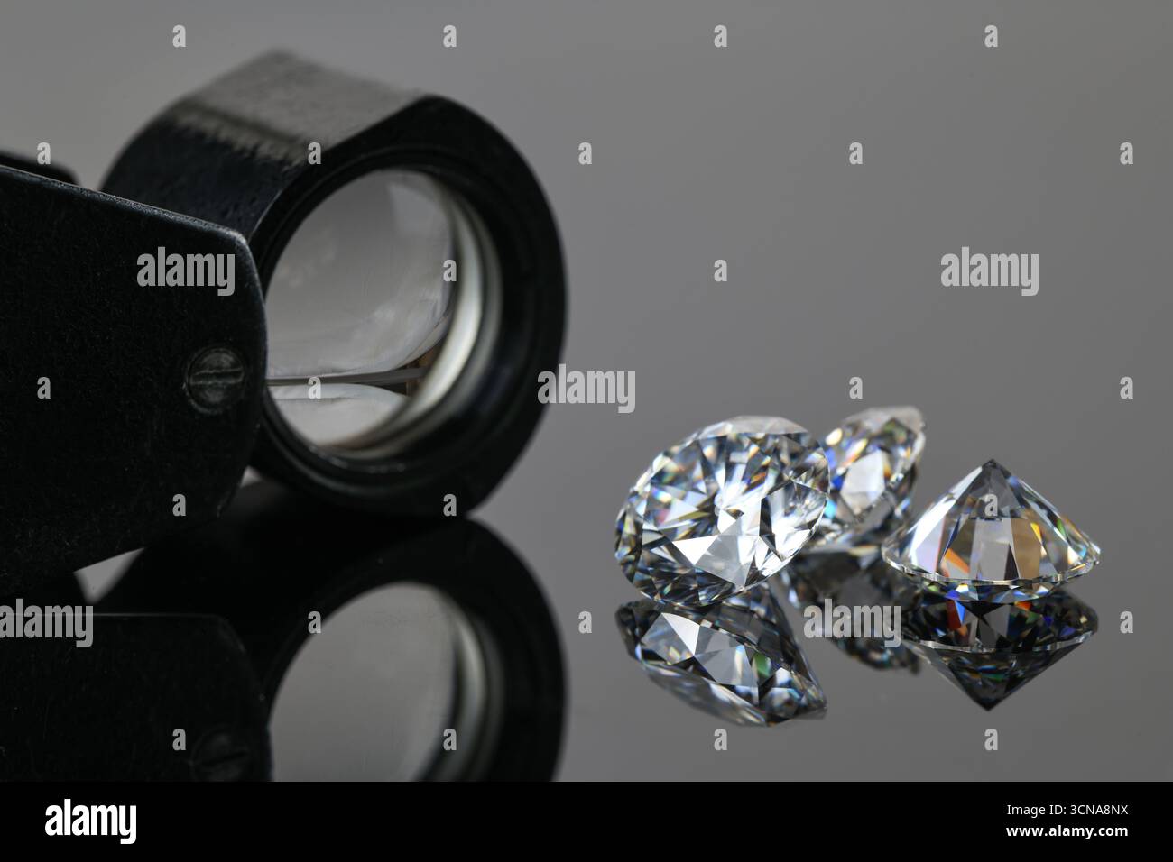 Una lente d'ingrandimento viene utilizzata per osservare tre diamanti. I diamanti hanno forme e dimensioni diverse Foto Stock