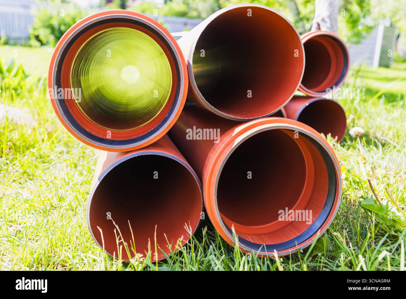 Una disposizione di nuove tubature arancioni impilate su una zona di lussureggiante erba verde all'aperto, vista concentrica. Rappresenta i temi della costruzione Foto Stock
