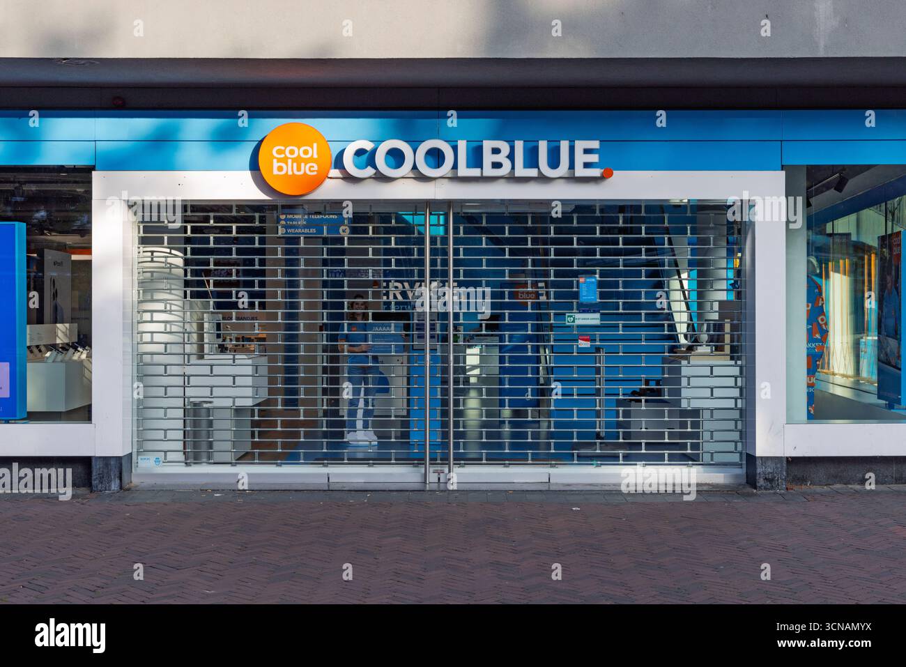Il punto vendita di un negozio di elettronica Coolblue, con una facciata blu e il nome del negozio, protetto da un otturatore di sicurezza chiuso. Rembrandt Theater in Foto Stock