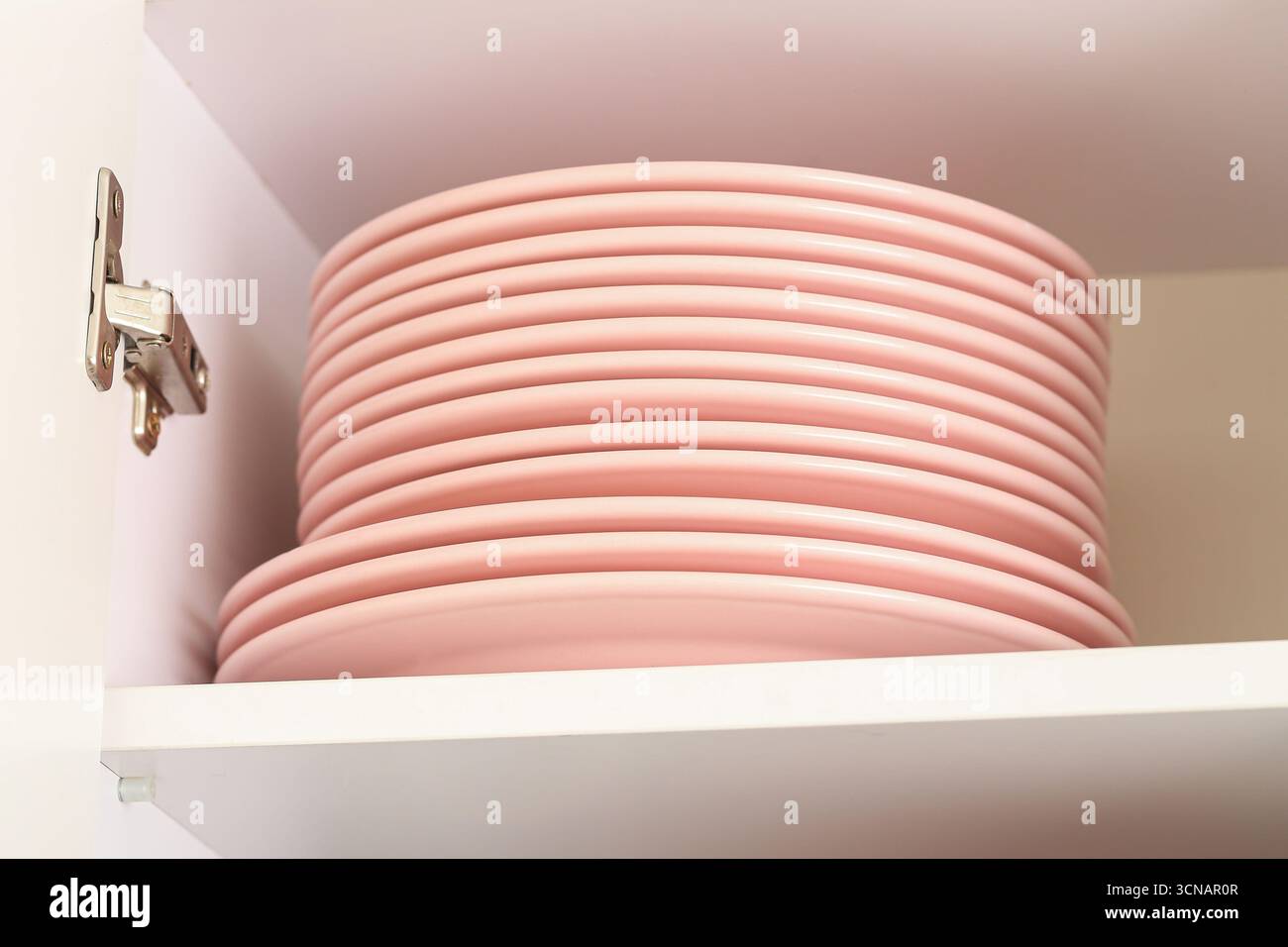 Piastre rosa impilate nell'armadio. Stoviglie da cucina disposte sullo scaffale. Organizzazione familiare impeccabile. Primo piano interno nazionale. Foto Stock