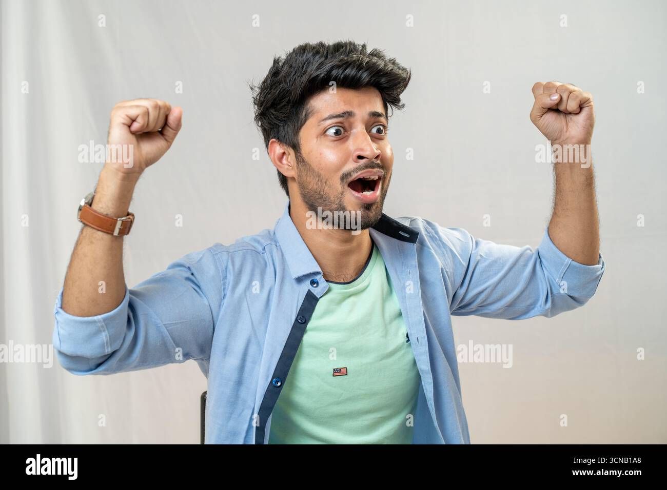 Un giovane festeggia con un pugno e un'espressione sorpreso e felice.uomo che festeggia con pugni allevati - Studio Portrait Foto Stock
