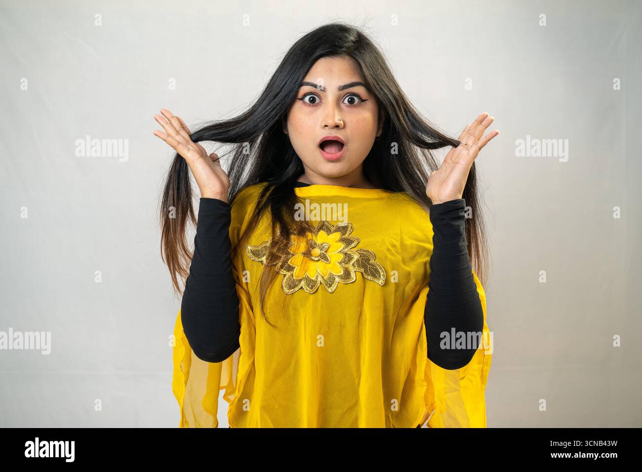 Una giovane donna con un'espressione scioccata che tiene i capelli in alto. Donna sorpresa con Top giallo - Studio Ritratto Foto Stock Una giovane donna con un'espressione scioccata che tiene i capelli in alto. Donna sorpresa con Top giallo - Studio Ritratto Foto Stock