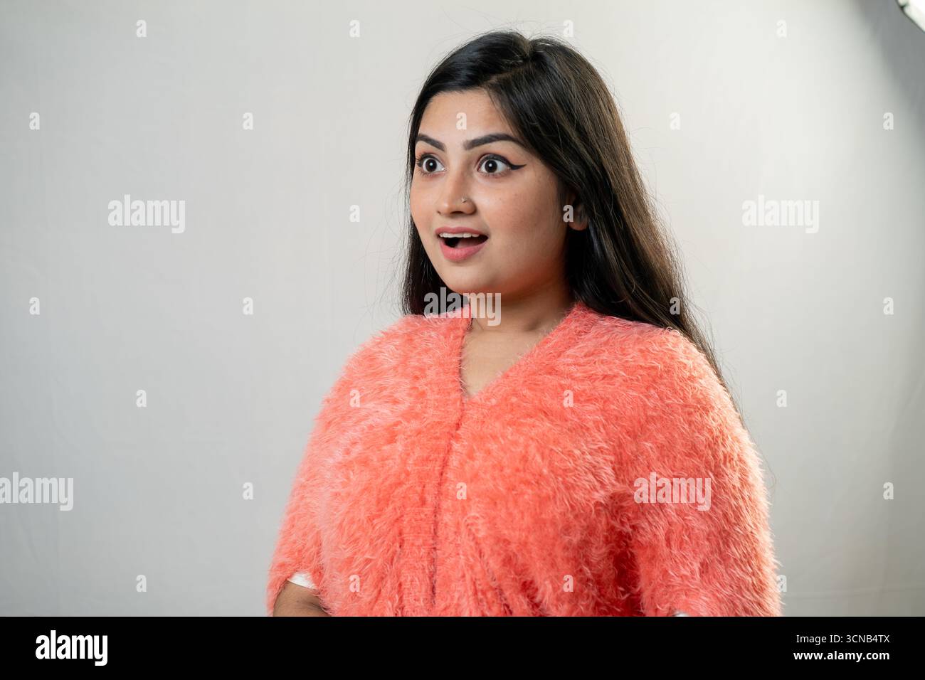 Una giovane donna con un'espressione felice e sorpresa, che guarda da parte. Foto Stock